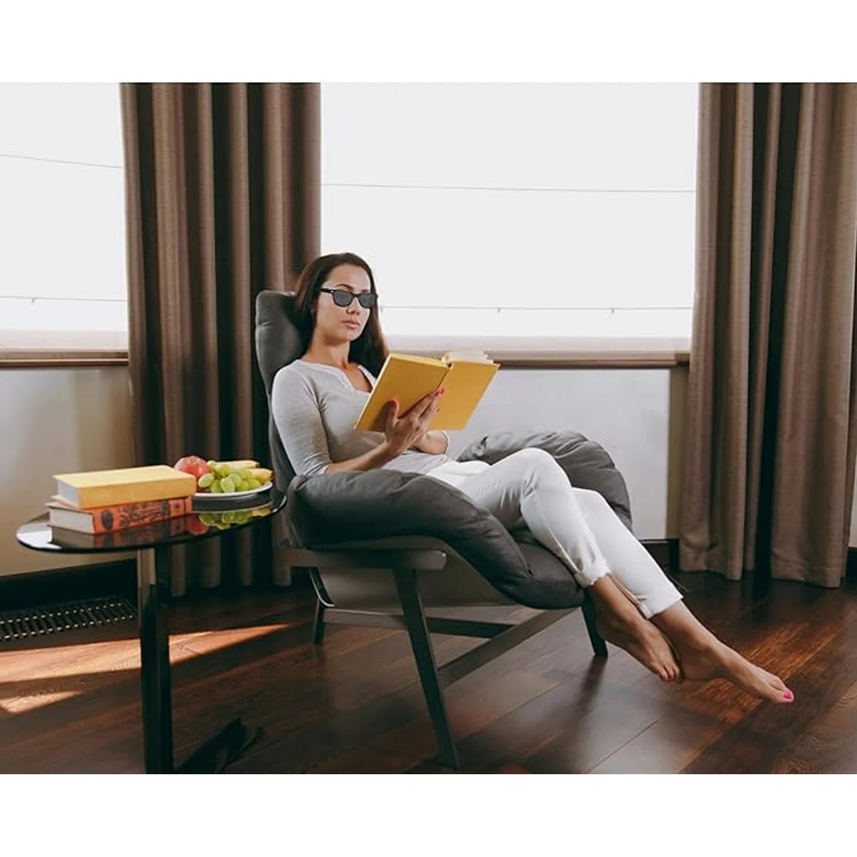 A woman in a living room wearing HopeLens pinhole glasses Classic model to read a book.